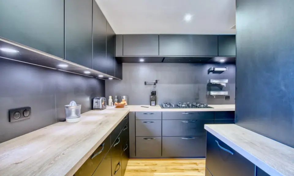 Cuisine moderne aux armoires sombres et plans de travail en bois. Une plaque de cuisson est installée, créant une cuisine sans hotte visible.