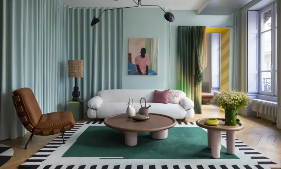 Un salon moderne avec un canapé blanc bouclé, un fauteuil en cuir marron, une table basse ronde et un tapis graphique. Une décoration appartement audacieuse et colorée.