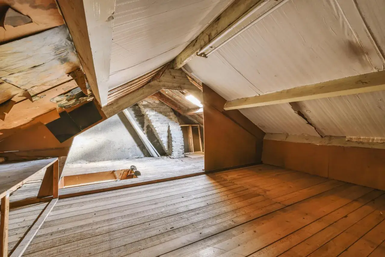 Espace brut sous les toits, prêt à aménager un grenier. Planchers de bois, poutres apparentes et murs en briques.