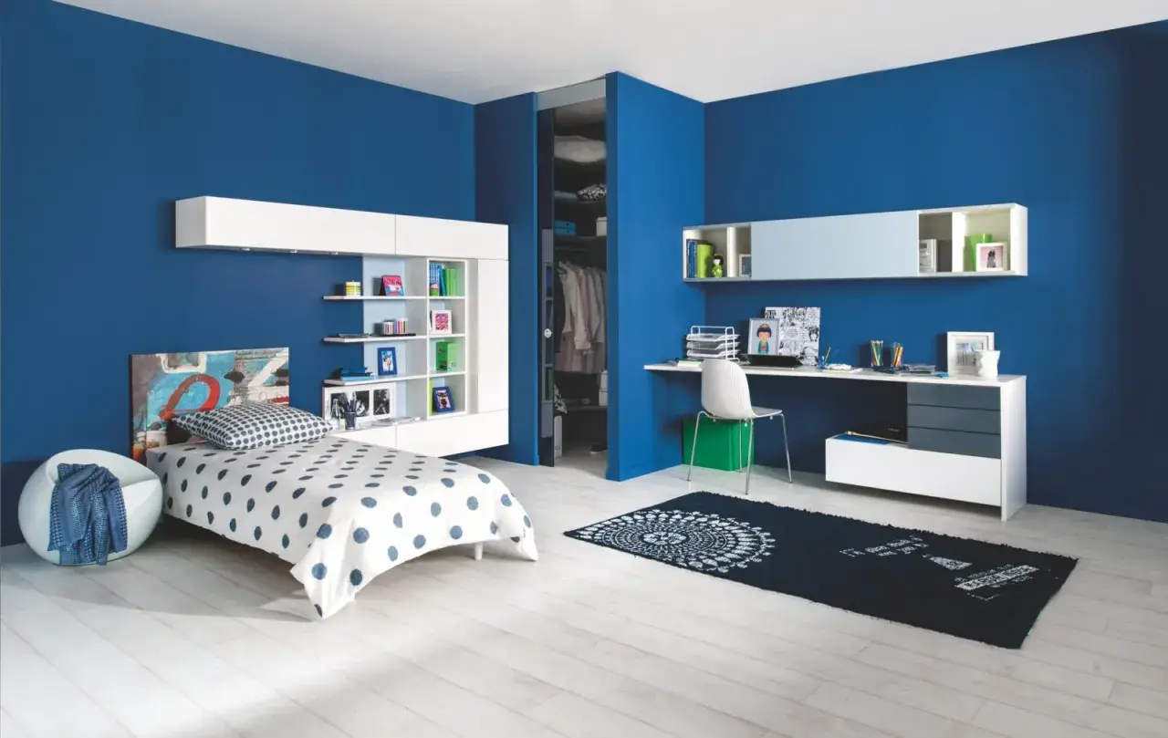Chambre d'enfant moderne aux murs d'un profond **couleur bleu**. Un lit blanc à pois bleus, une étagère murale et un bureau complètent l'espace.
