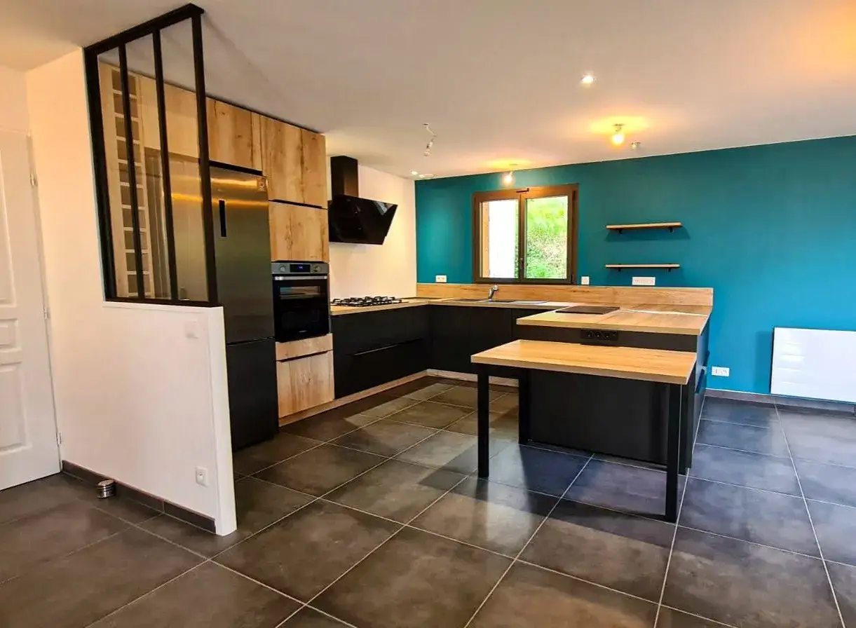 Cuisine moderne en 2 parties, avec &icirc;lot central en bois et noir, murs bleu canard et &eacute;l&eacute;ments en bois clair.