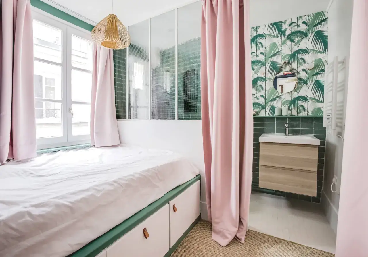 Comment amenager une chambre en longueur : lit bas avec rangements, rideaux roses, verri&egrave;re et coin lavabo avec papier peint tropical.