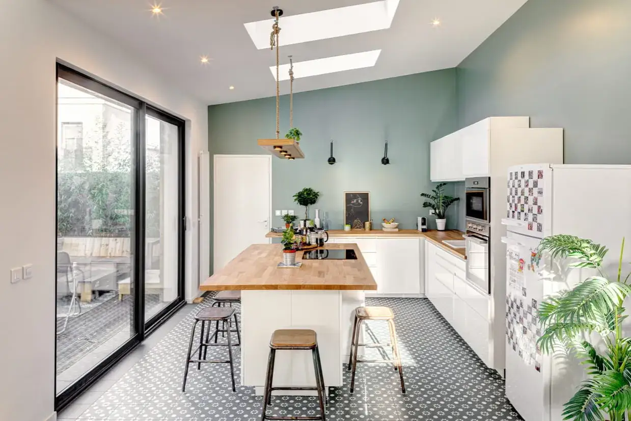 Cuisine moderne aux murs vert d'eau et plan de travail en bois. L'&icirc;lot central en bois massif invite &agrave; la convivialit&eacute;.