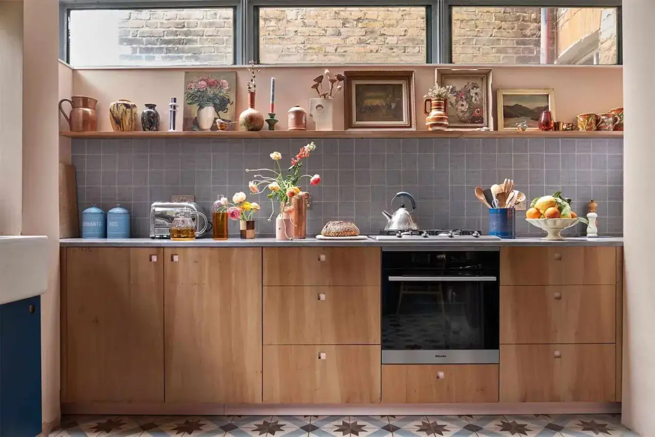 Cuisine avec placards en bois clair, plan de travail gris, carrelage mural gris. Un grille-pain, des pots, des fleurs et une bouilloire sont disposés pour organiser le plan de travail cuisine.