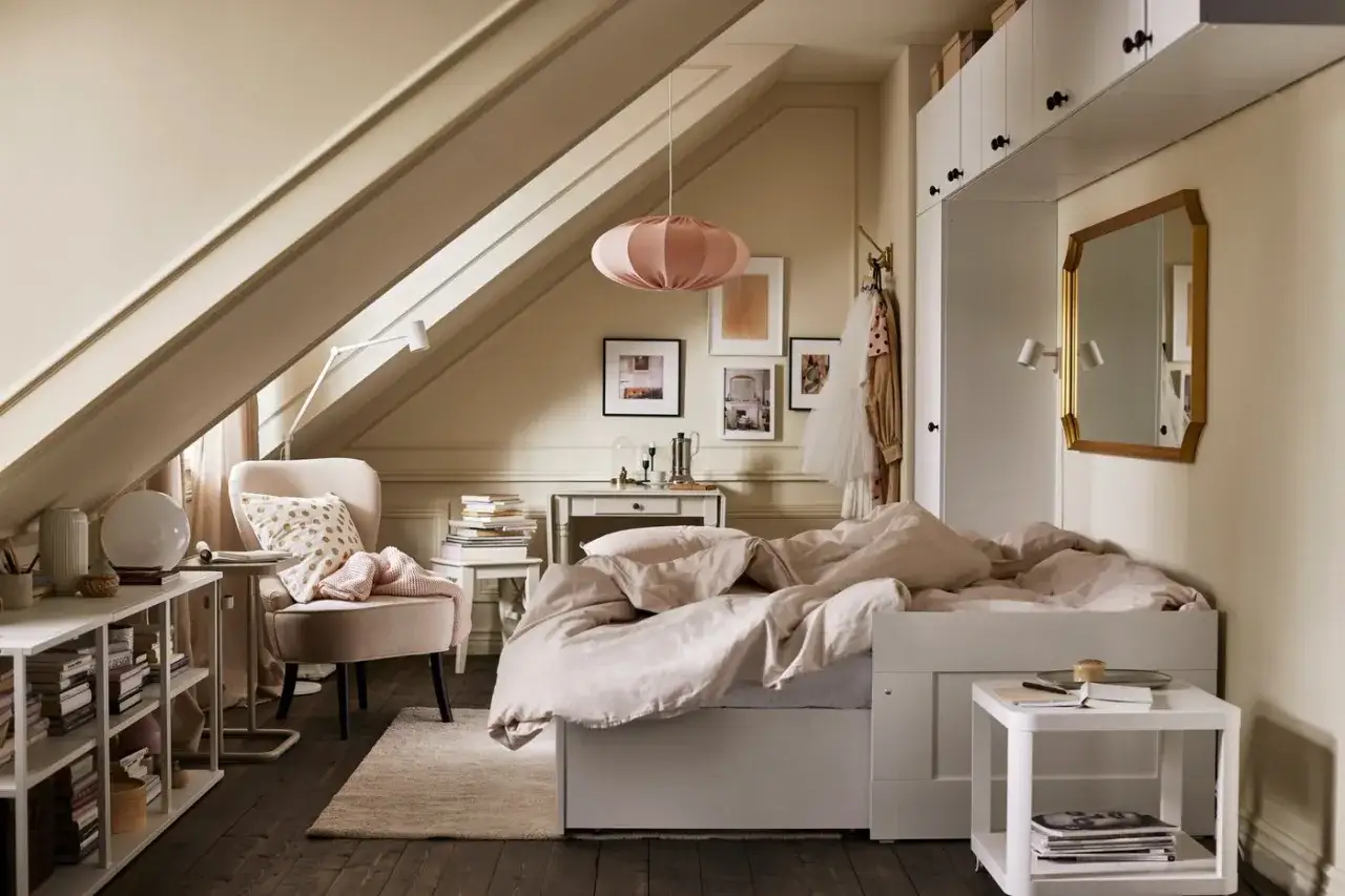 Chambre mansard&eacute;e avec un lit sous pente douillet, un fauteuil confortable et une &eacute;tag&egrave;re remplie de livres.