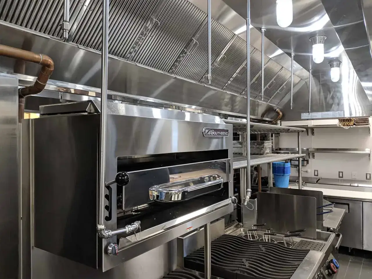 Une cuisine professionnelle moderne avec un four &agrave; pizza Southbend et une friteuse, sous une grande hotte aspirante en acier inoxydable.