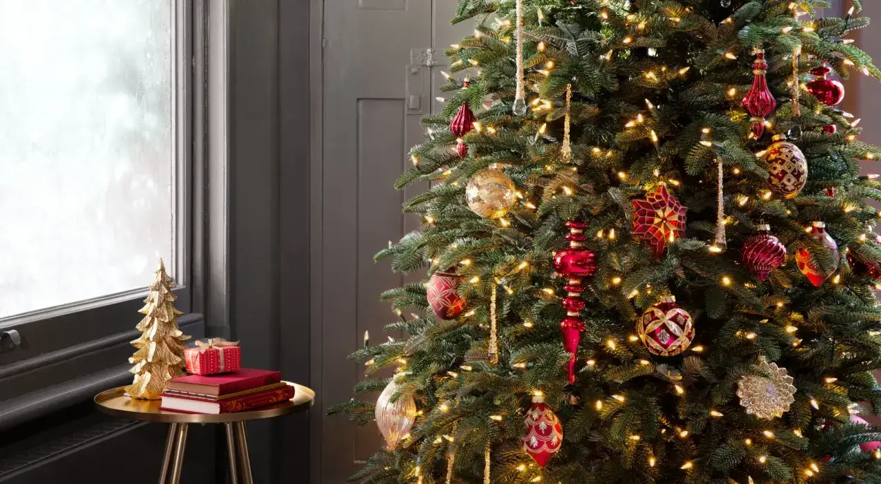 Comment faire un beau sapin : un arbre de No&euml;l d&eacute;cor&eacute; de boules rouges et dor&eacute;es, de guirlandes lumineuses et d'ornements scintillants. &Agrave; c&ocirc;t&eacute;, une petite table avec un sapin dor&eacute; et des cadeaux.