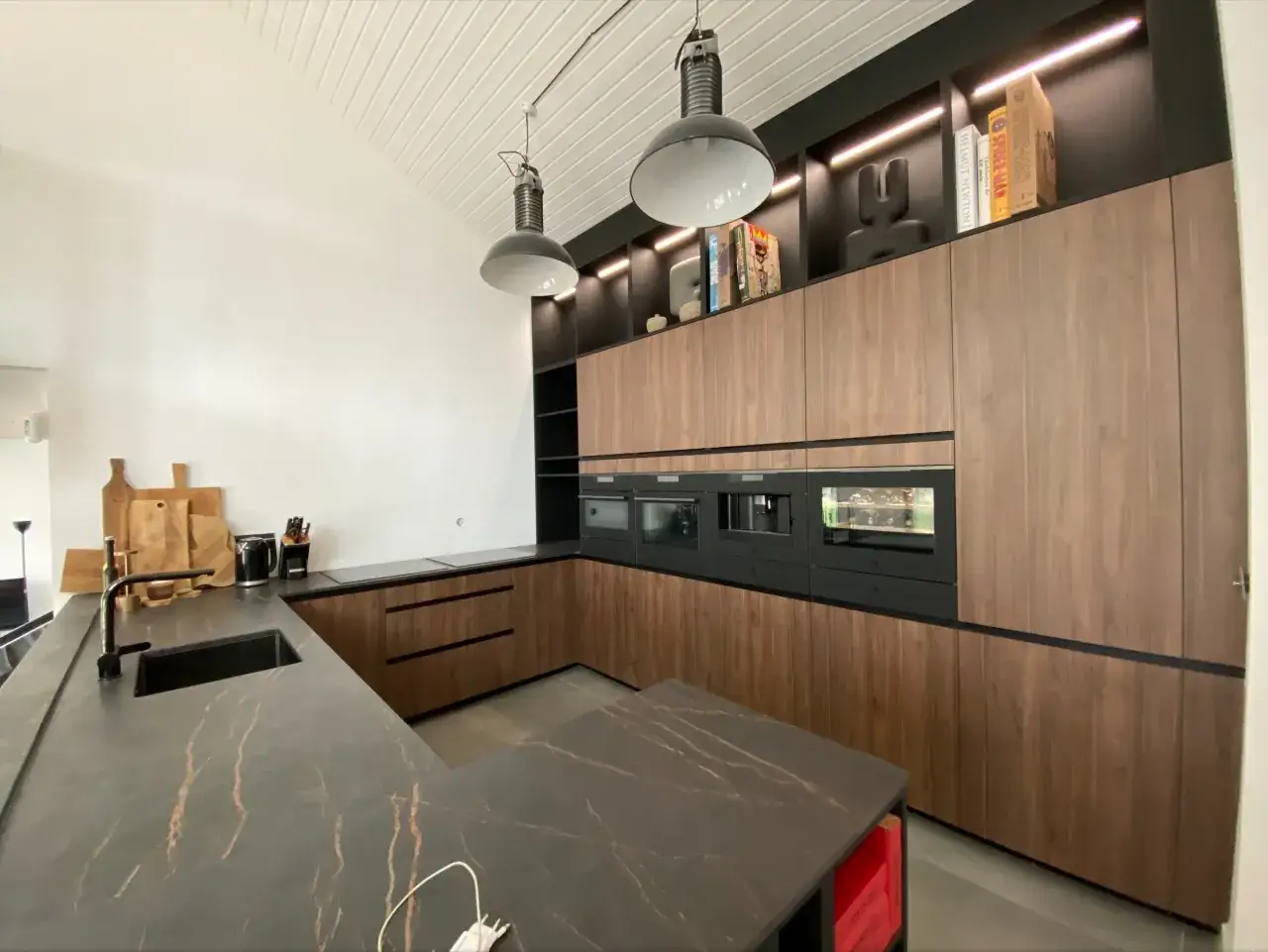 Plan cuisine moderne avec &icirc;lot central, plan de travail en marbre noir vein&eacute;, meubles en bois, &eacute;lectrom&eacute;nagers int&eacute;gr&eacute;s et &eacute;clairage d'ambiance.