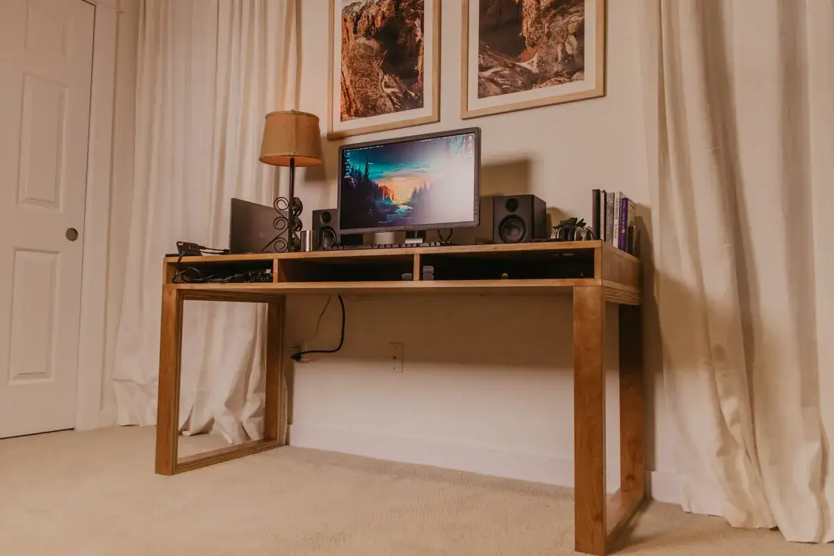 Un bureau DIY en bois clair, avec un &eacute;cran d'ordinateur, des enceintes, une lampe et des livres.