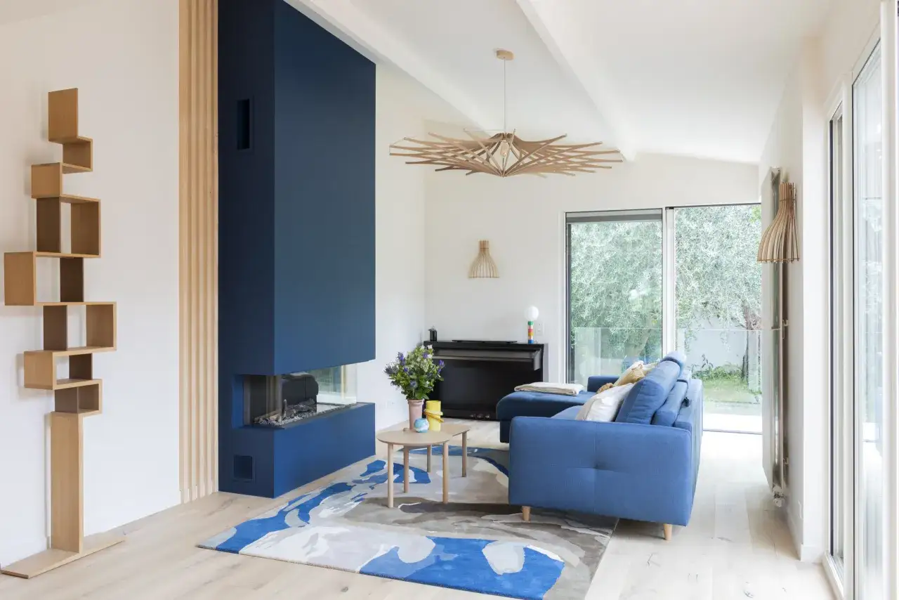 Canapé et cheminée d'angle d'un profond couleur bleu, dans un salon moderne avec étagère en bois et tapis abstrait.