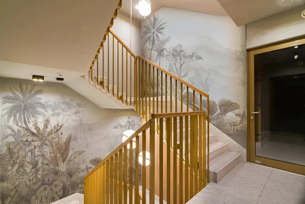 Cage d'escalier avec un papier peint jungle et des rampes dorées. Quelle couleur choisir pour peindre une cage d'escalier ? Ici, le doré s'harmonise avec le décor.