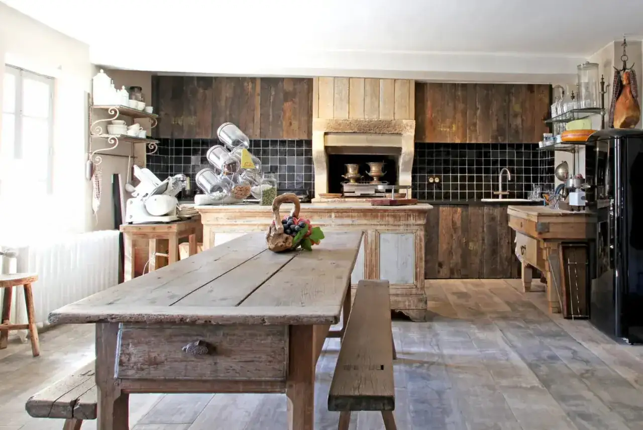 Ambiance chaleureuse d'une cuisine campagne chic avec table en bois brut, îlot central patiné et murs en bois vieilli.
