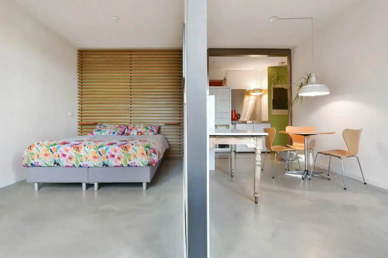 Am&eacute;nagement d'un studio 30m2 en 2 pi&egrave;ces : chambre avec lit fleuri et espace cuisine/salle &agrave; manger.