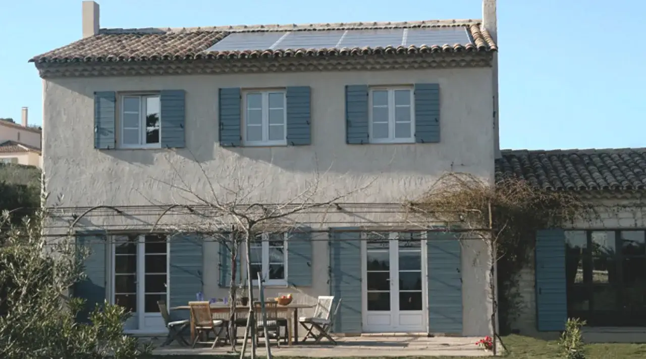Maison de style de maison ancienne avec volets bleus, panneaux solaires sur le toit et une table de jardin.