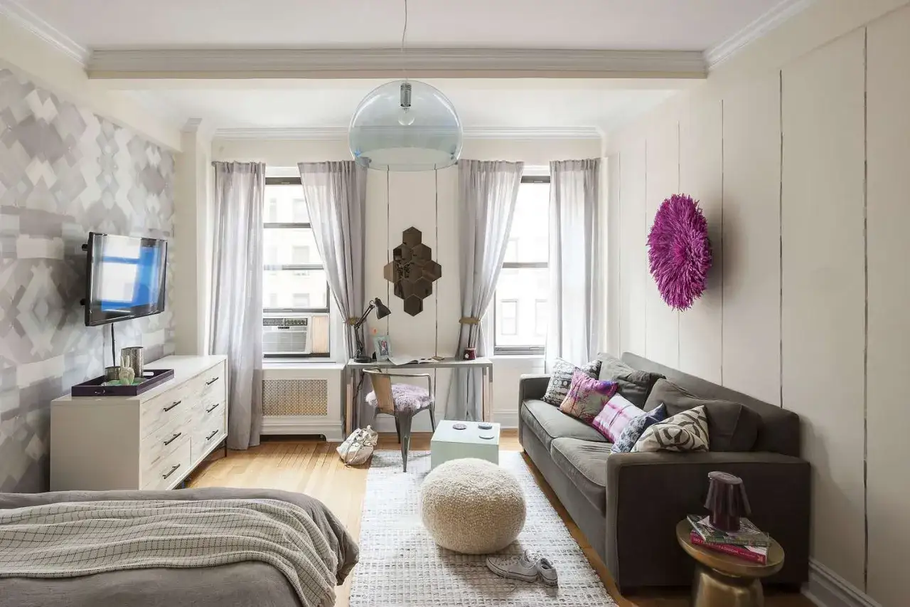 Aménagement studio fonctionnel avec lit, canapé, bureau et rangements. Décoration murale géométrique et coussins colorés.