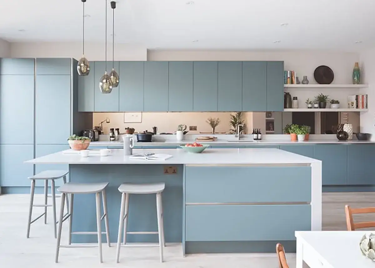Cuisine moderne aux armoires bleu glacier, &icirc;lot central avec tabourets, et &eacute;tag&egrave;res d&eacute;cor&eacute;es.