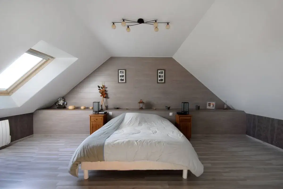 Chambre am&eacute;nag&eacute;e sous les toits, un lit douillet, des tables de nuit en bois. Ce plan d'am&eacute;nagement combles optimise l'espace.