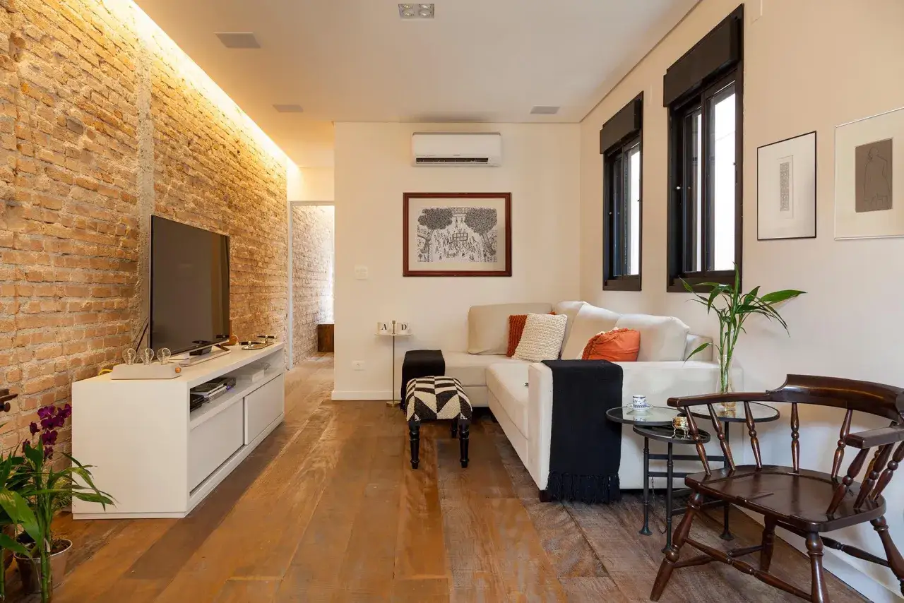 Salon moderne avec mur en briques apparentes, canap&eacute; confortable et parquet. Une maison en longueur bien am&eacute;nag&eacute;e pour la d&eacute;tente.