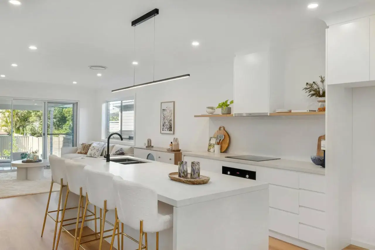 Un modèle de cuisine simple et lumineux avec un îlot central, des tabourets blancs et dorés, et une vue sur le salon.