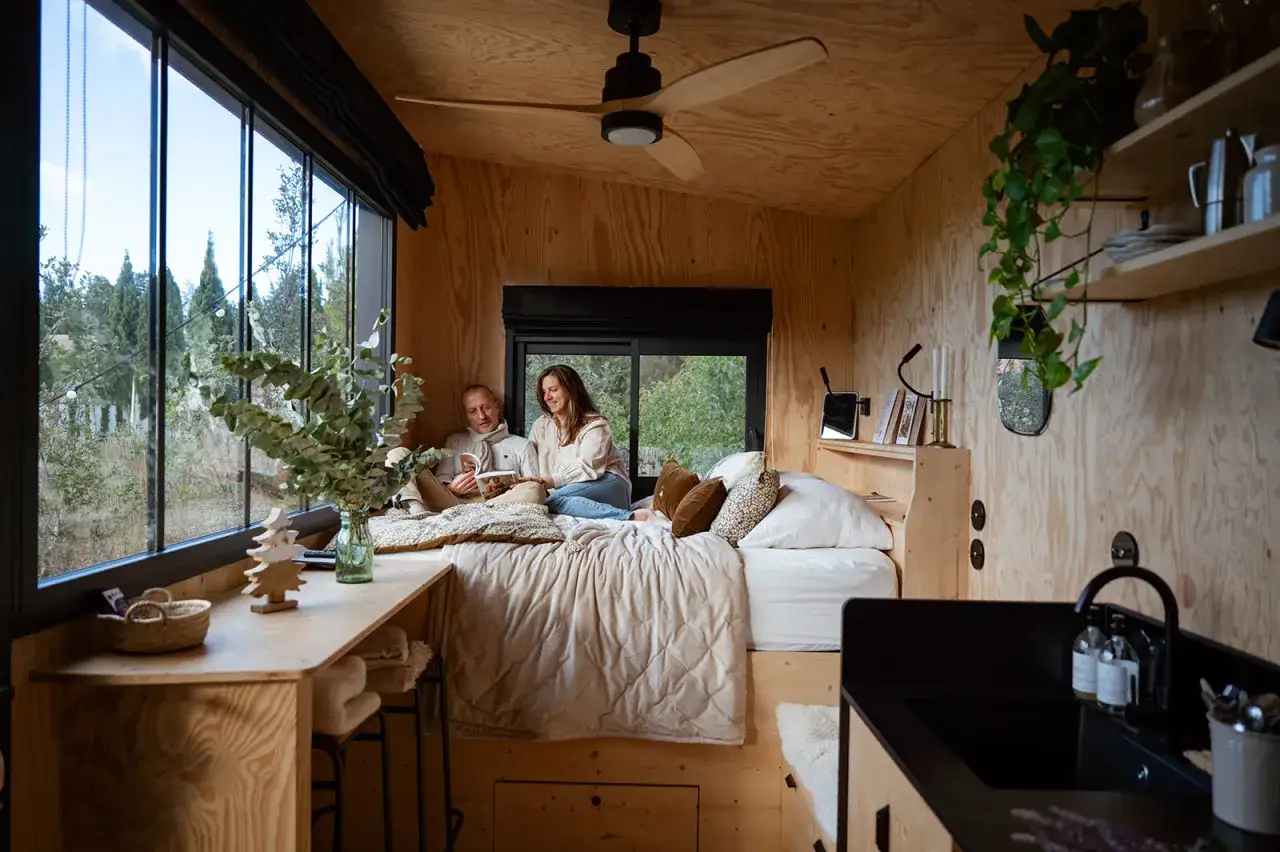 Un couple lit dans un lit douillet, profitant du tiny house interieur chaleureux et lumineux avec vue sur la nature.