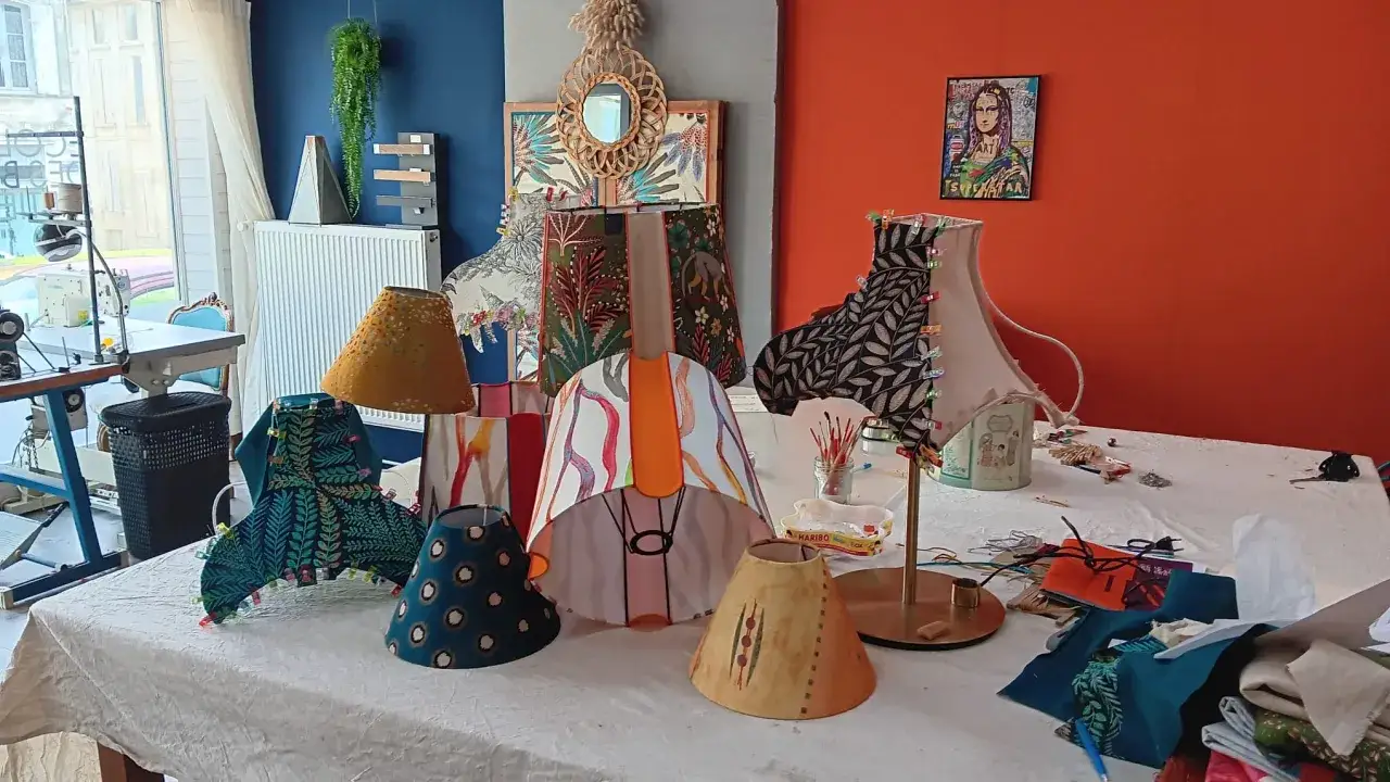 Atelier de cr&eacute;ation d'abat jour DIY. Divers abat-jour aux motifs vari&eacute;s, tissus, fils et mat&eacute;riel de couture sur une table.