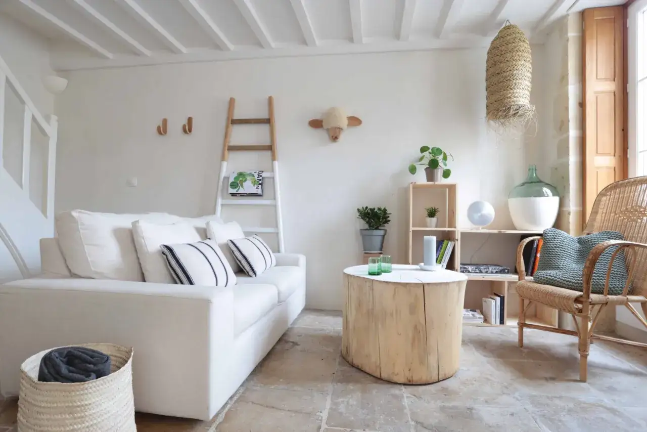 Salon lumineux d'une maison de p&ecirc;cheur, avec canap&eacute; blanc, table en tronc d'arbre et fauteuil en rotin.