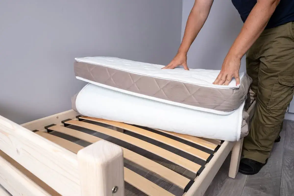 Un homme montre comment plier un matelas en le superposant sur un sommier en bois.