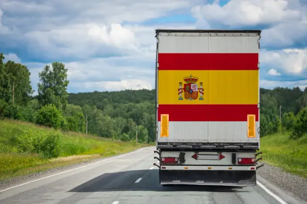 Camion aux couleurs de l'Espagne sur une route de campagne, prêt à déménager en Espagne. Paysage verdoyant sous un ciel nuageux.