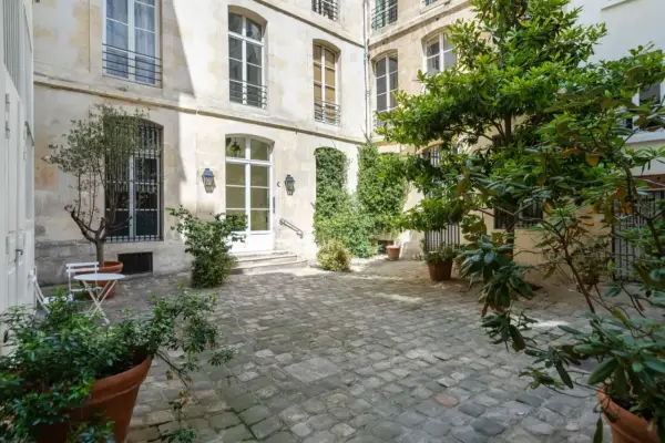 Cour pavée d'un immeuble parisien, avec un petit olivier et une table. Idéal pour un projet de déménager à Paris et profiter de la douceur de vivre.