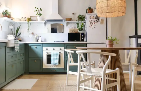 Cuisine verte avec four blanc, îlot central en bois et chaises blanches. Un modèle de cuisine simple et chaleureux.