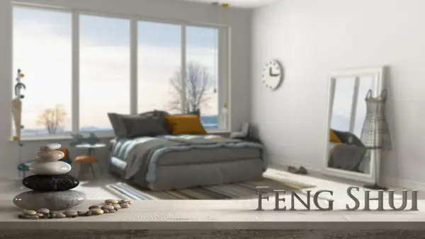 Une chambre apaisante avec un lit douillet, une pile de galets et le mot "FENG SHUI" en lettres métalliques.