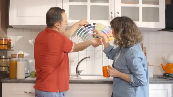 Un couple choisit des couleurs pour peindre le carrelage de sa cuisine, tenant un éventail de nuanciers.