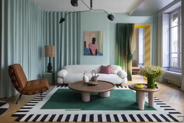 Un salon moderne avec un canapé blanc bouclé, un fauteuil en cuir marron, une table basse ronde et un tapis graphique. Une décoration appartement audacieuse et colorée.