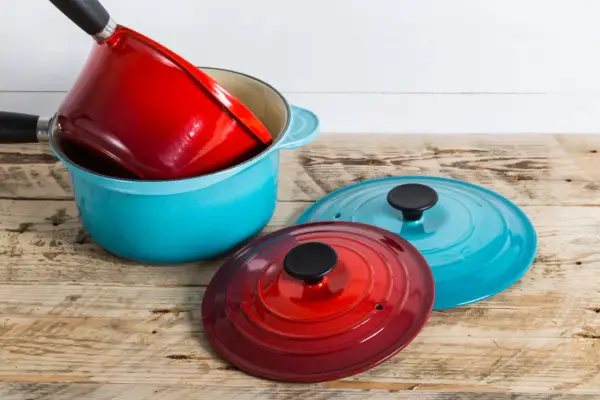 Une astuce rangement casserolier : une cocotte bleue empilée avec une rouge à l'intérieur, et deux couvercles colorés à côté.