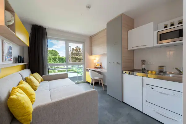Aménagement studio moderne avec canapé, coin cuisine, bureau et vue sur jardin.