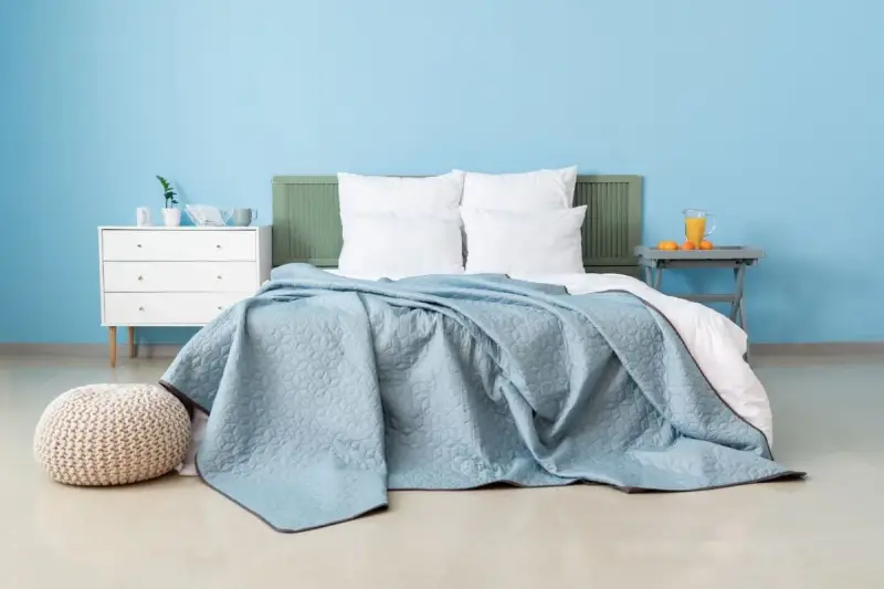 Une chambre paisible avec un lit douillet recouvert d'une couverture bleu glacier. Un pouf moelleux et une commode blanche complètent l'ensemble.