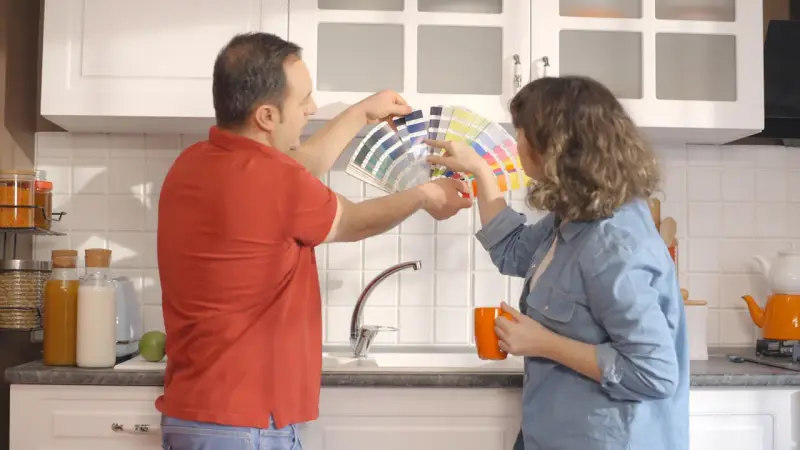 Un couple choisit des couleurs pour peindre le carrelage de sa cuisine, tenant un éventail de nuanciers.